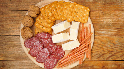 Meat and cheese plate for appetizers. Sausages, cheeses, crackers, nuts on a wooden plate and background. Top view.