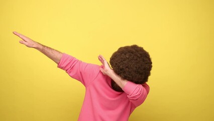 Man with Afro hairstyle with positive expression dabbing raising hands, making dubdance gesture, showing dab dance pose, wearing pink sweatshirt. Indoor studio shot isolated on yellow background.