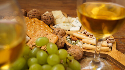 Snacks for wine. Cheese plate. Cheese, nuts, grapes, crackers on wooden background. Blurred foreground with two glasses of white wine.