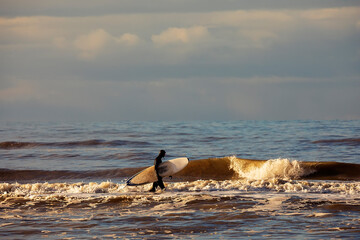 surfer with board walking in sea waves