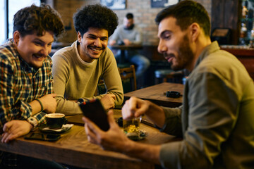 Multiracial group of men has fun while using mobile phone in cafe.