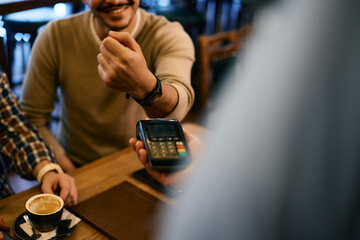 Close-up of  male guest paying contactless with smart watch in a cafe.