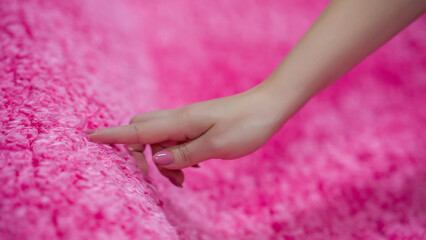 Woman touching a pink carpet close-up. Close-up of a hand touching a soft carpet. Gentle and fluffy carpet between the fingers.