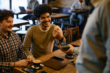 Young Muslim man using smart watch while paying bill in a pub.
