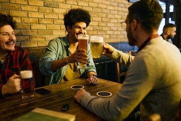 Multiracial group of men toast with beer and have fun while gathering in pub.