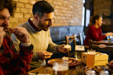 Young man eats while gathering with friends for lunch in a pub.