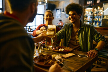 Happy multiracial couple and their friends toast with beer and have fun during lunch in pub.