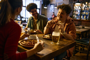 Happy man eats ribs and talks with his friends during their lunch in a pub.