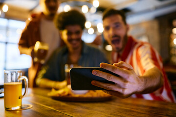 Close up of male friends watching soccer game on smart phone in a bar.