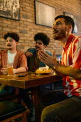 Multiracial group of young sports fans watching match on TV in a pub.