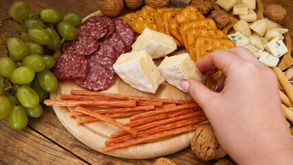 A woman hand takes a piece of Camembert cheese from a cheese plate. Italian cheese and meat platter...
