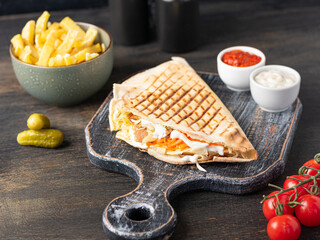 Pita shawerma with vegetables and yogurt sauce on dark wooden background. Levantine cuisine