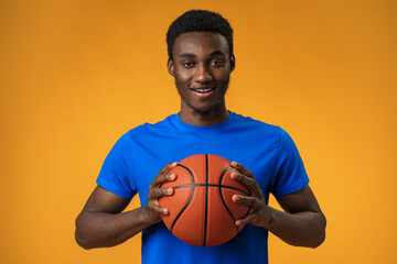 Portrait of a smiling young African American man holding a basketball on yellow background