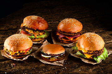 A set of homemade delicious burgers of beef, bacon, cheese, lettuce and tomatoes on a dark...