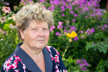 Portrait of woman 60s years old against background of flowers in garden