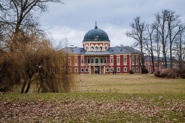 Veltrusy, Central Bohemia, Czech Republic, 5 January 2022: Rococo castle with park and garden, Romantic baroque chateau red with white windows in sunny day, green wooden shutters on windows