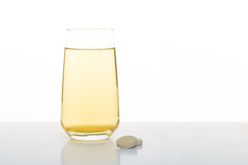 Glass with yellow water. Vitamin drink in a glass. A glass and a tablet on a white background.