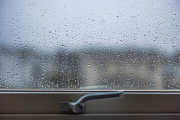 Close up macro shot of raindrops on window pane with blurry view of neighboring houses through wet rainy window. Sweden.