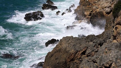 Crystal clear turquoise water, waves crashing on the rocky shore, and the ruins
