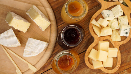 Jars of homemade jams and honey and a variety of cheeses on a wooden table. Cheese plate for appetizers with wooden skewers for food. Top view
