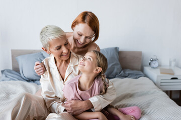 Woman hugging girlfriend in pajamas and child on bed