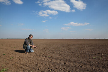 Fototapeta na wymiar Farmer or agronomist inspecting cultivated ground in field after sowing, and typing to tablet, agricultural works in spring