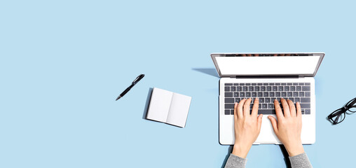 Person using a laptop computer with a notebook and eyeglasses - Flat lay - obrazy, fototapety, plakaty