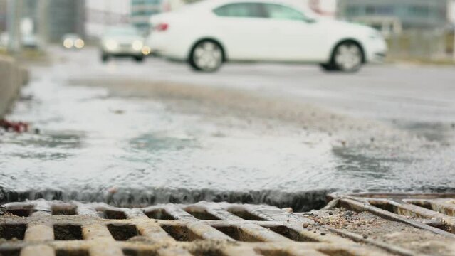 Melted water flows down to sewer grate on urban road with vehicle traffic at spring time