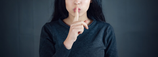 woman showing a sign of silence gesture putting finger in mouth - obrazy, fototapety, plakaty