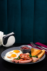 Full English Breakfast on dark table sausage eggs bean bacon tomatos mushroom
