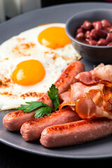 Full English Breakfast on dark table sausage eggs bean bacon tomatos mushroom