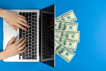Fototapeta na wymiar Female hands on laptop keyboard with money. Freelance concept, making money at home. Modern workspace, flat lay, blue background and top view photo