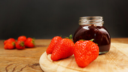 Strawberry jam in the glass jar with fresh berries on wooden background. Close up photo. Ingredients for making delicious breakfast