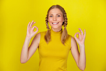 Portrait of happy smiling woman wearing yellow t-shirt showing OK sign against colored background