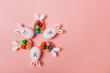 Top view Easter pink background with flower shape made of funny eggs containers with bunny ears filled with candy chocolate eggs. Bunny rabbit symbol. Easter egg hunt. Creative Easter. Copy space.
