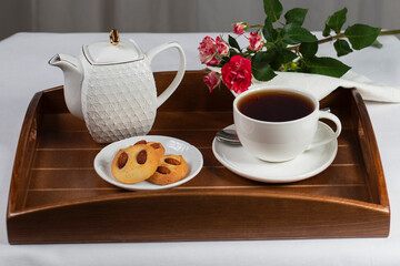 a cup of tea with cookies and a rose on a tray
