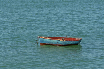 Naklejka na ściany i meble Old worn blue and red dinghy in the sea