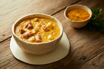 Mote pata is a traditional ecuadorian soup made from mote, pork, sausage and sambo seeds. It’s served on a white plate with a rustic, wooden and homey background. 