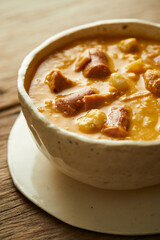 Mote pata is a traditional ecuadorian soup made from mote, pork, sausage and sambo seeds. It’s served on a white plate with a rustic, wooden and homey background. 