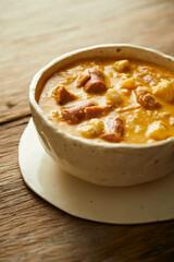 Mote pata is a traditional ecuadorian soup made from mote, pork, sausage and sambo seeds. It’s served on a white plate with a rustic, wooden and homey background. 