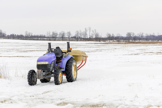Peri colored tractor sits idle in field during winter with snow on the ground