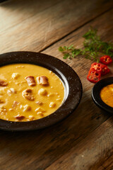 Mote pata is a traditional ecuadorian soup made from mote, pork, sausage and sambo seeds. It’s served on a white plate with a rustic, wooden and homey background. 