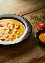 Mote pata is a traditional ecuadorian soup made from mote, pork, sausage and sambo seeds. It’s served on a white plate with a rustic, wooden and homey background. 
