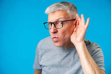 Middle age man over iblue background with hand over ear listening