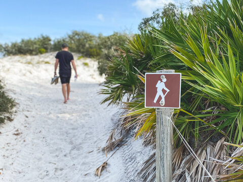 Coastal environment, sandy beach hiking trail, man in background walking barefoot in the sand. Nature path, wildlife refuge, state parks.