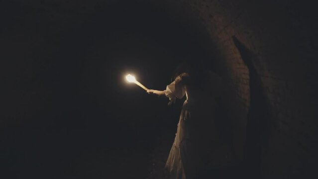 Woman with a torch in a vintage dress Runs through a medieval vVII century tunnel dungeon with brick vaults and a river.