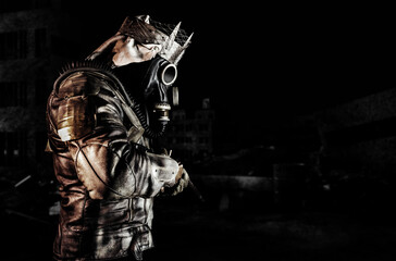 Fototapeta na wymiar Photo of post apocalyptic warrior with armored outfit jacket and scrap crown standing side view with rifle on dark destroyed city background.