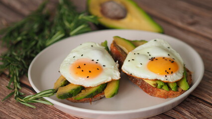 Two Toasts with avocado and fried egg, rosemary. Preparing healthy avocado toast for breakfast with avocado slices rye wholegrain bread and sunny side up egg on top. Healthy breakfast for two, couple