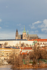 Fototapeta premium The Prague castle the river and the threatening sky. The castle and the historic quarter are lit up, the sky is threatening black. The Vltava flows towards the red roofs of the buildings.