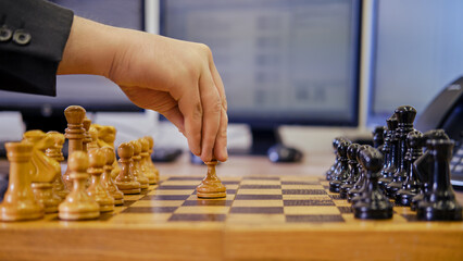 A businessman man with a chess piece pawn in his hands is working on a computer keyboard at an...